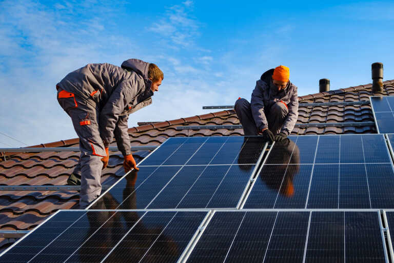 2 eco heat shop workers are installing a solar panels at roof.